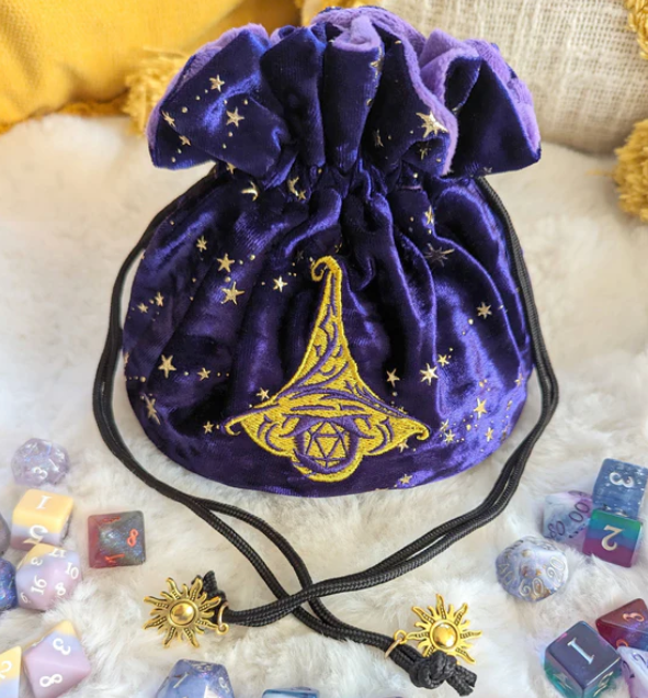 This wizard multi pocket dice bag is made with starry purple velvet and matching plush fabric. It is soft to the touch and will keep your dice nice and cozy. The embroidered design on the front features a large wizard hat with a D20 underneath it. The bag has strong cord drawstrings accented with golden sun charms at the ends.